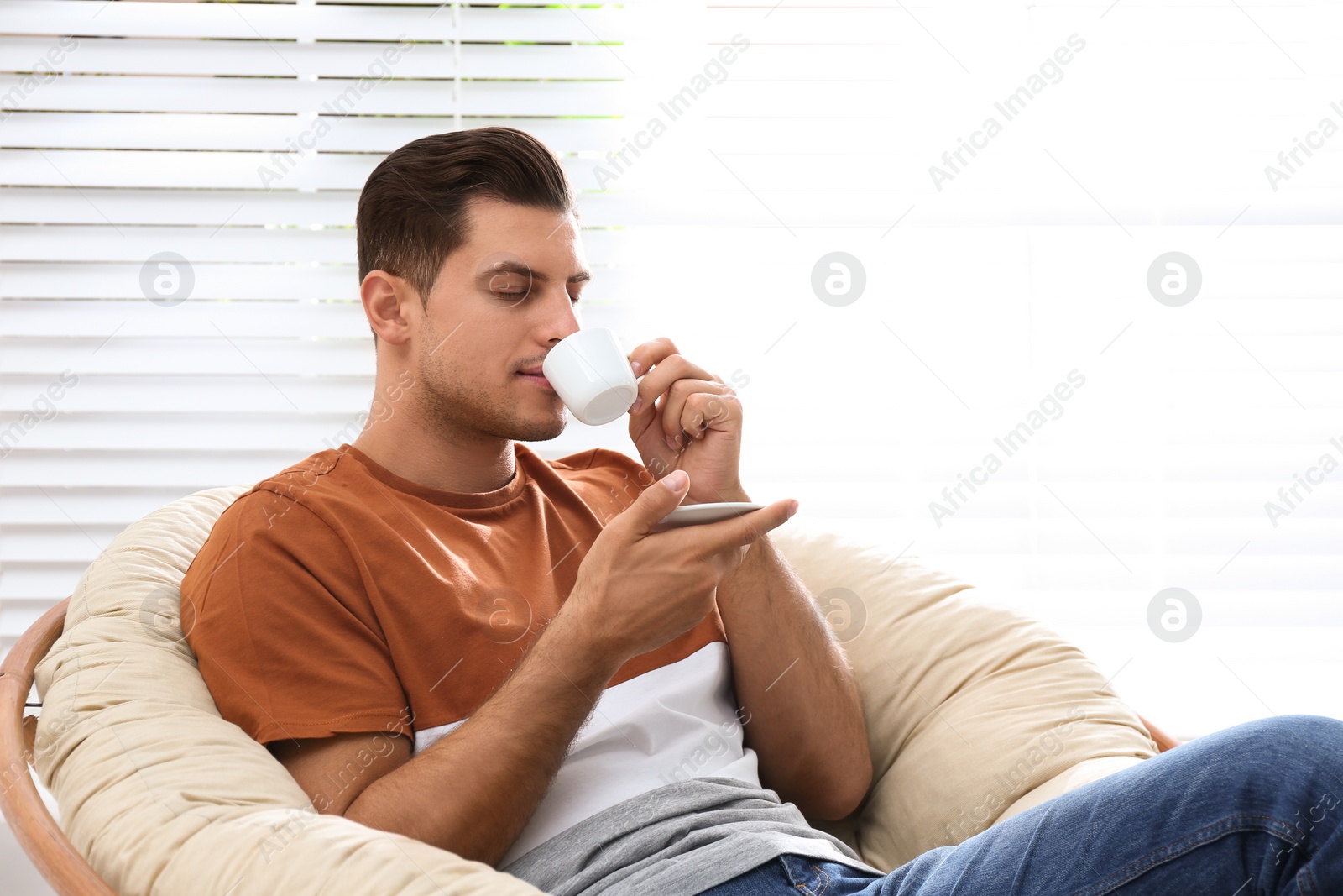 Photo of Attractive man relaxing in papasan chair near window at home