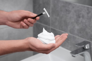 Photo of Man holding shaving foam and razor in bathroom, closeup