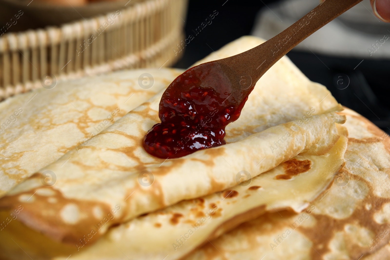 Photo of Putting jam on stack of fresh thin pancakes, closeup