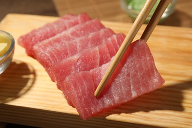 Photo of Taking tasty sashimi (piece of fresh raw tuna) from wooden board, closeup
