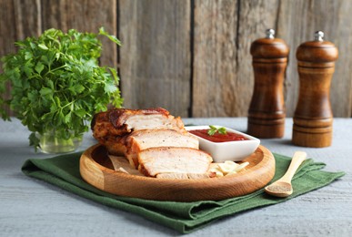 Photo of Pieces of baked pork belly served with sauce on grey wooden table