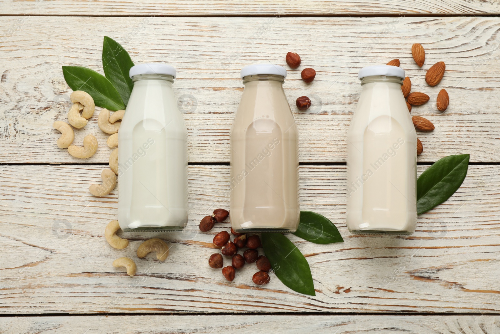 Photo of Different vegan milks and nuts on white wooden table, flat lay