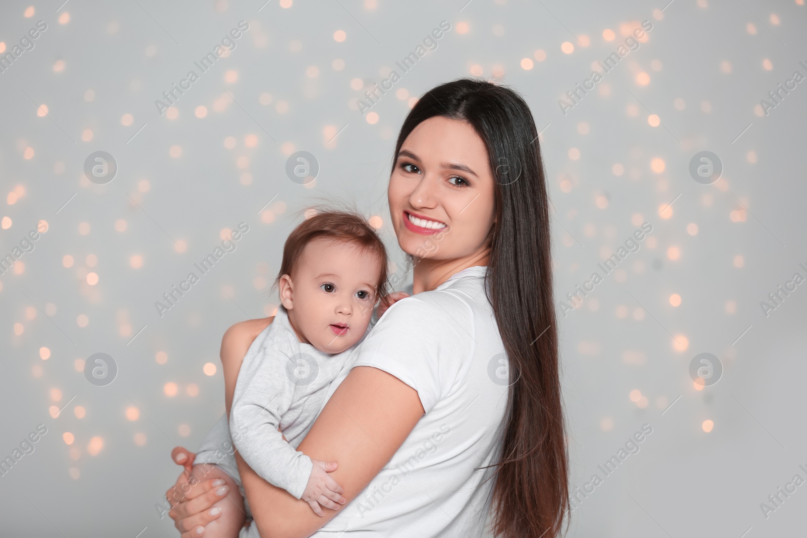 Photo of Portrait of young mother and her adorable baby against defocused lights