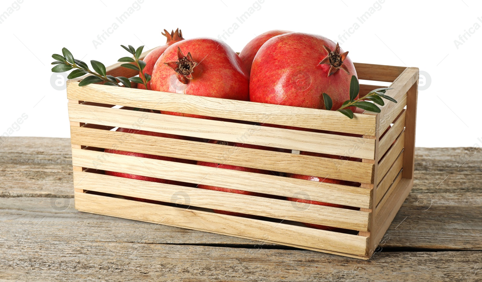 Photo of Fresh pomegranates and green leaves in box on wooden table against white background