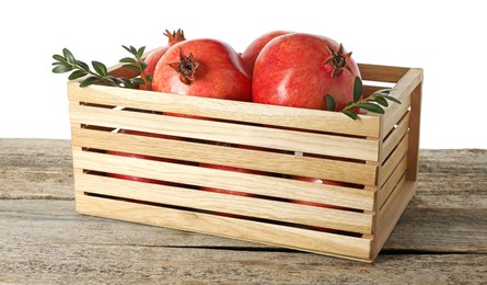 Fresh pomegranates and green leaves in box on wooden table against white background