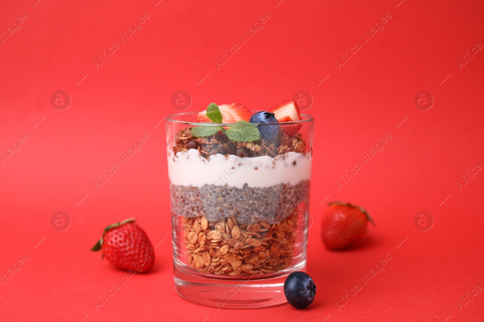 Photo of Tasty granola with berries, yogurt and chia seeds in glass on red background