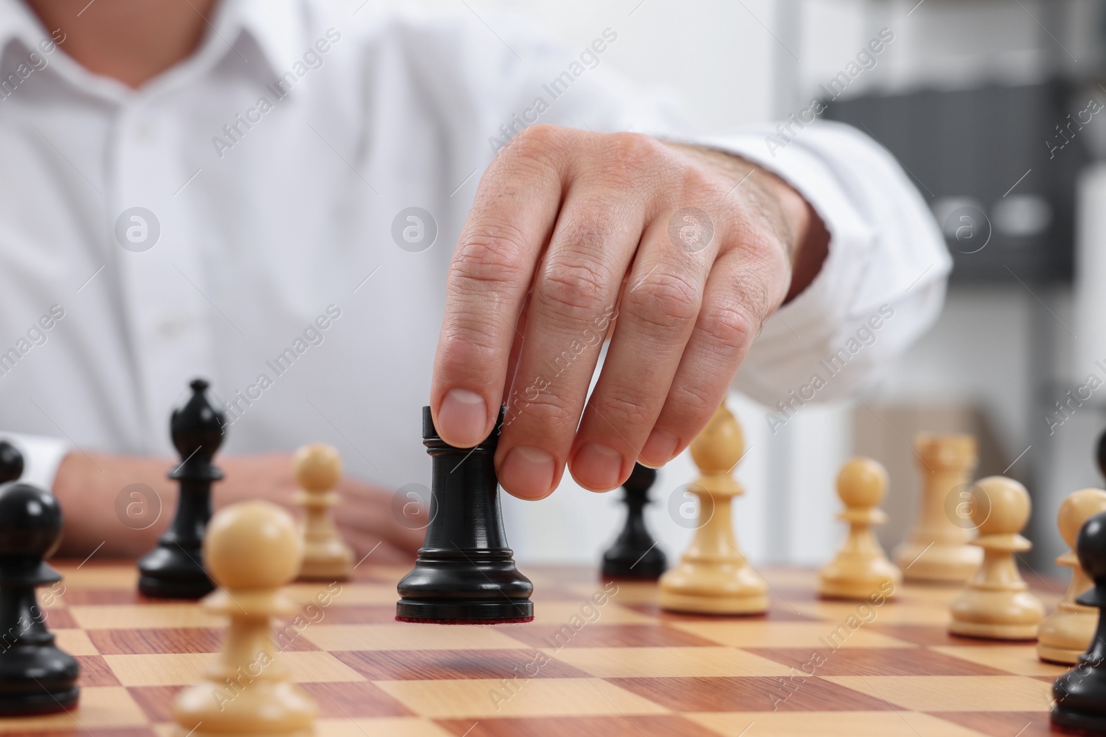 Photo of Man with rook game piece playing chess at checkerboard indoors, closeup