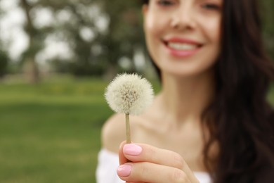 Photo of Beautiful young woman holding dandelion outdoors, focus on hand with flower. Allergy free concept