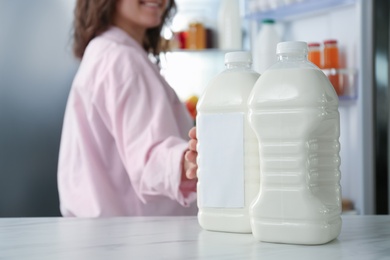 Photo of Young woman taking gallon of milk from table in kitchen, closeup