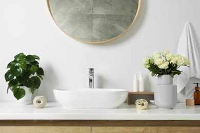 Photo of Vase with beautiful white roses and toiletries near sink in bathroom