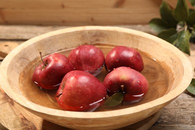 Photo of Fresh red apples in bowl with water on wooden table, closeup