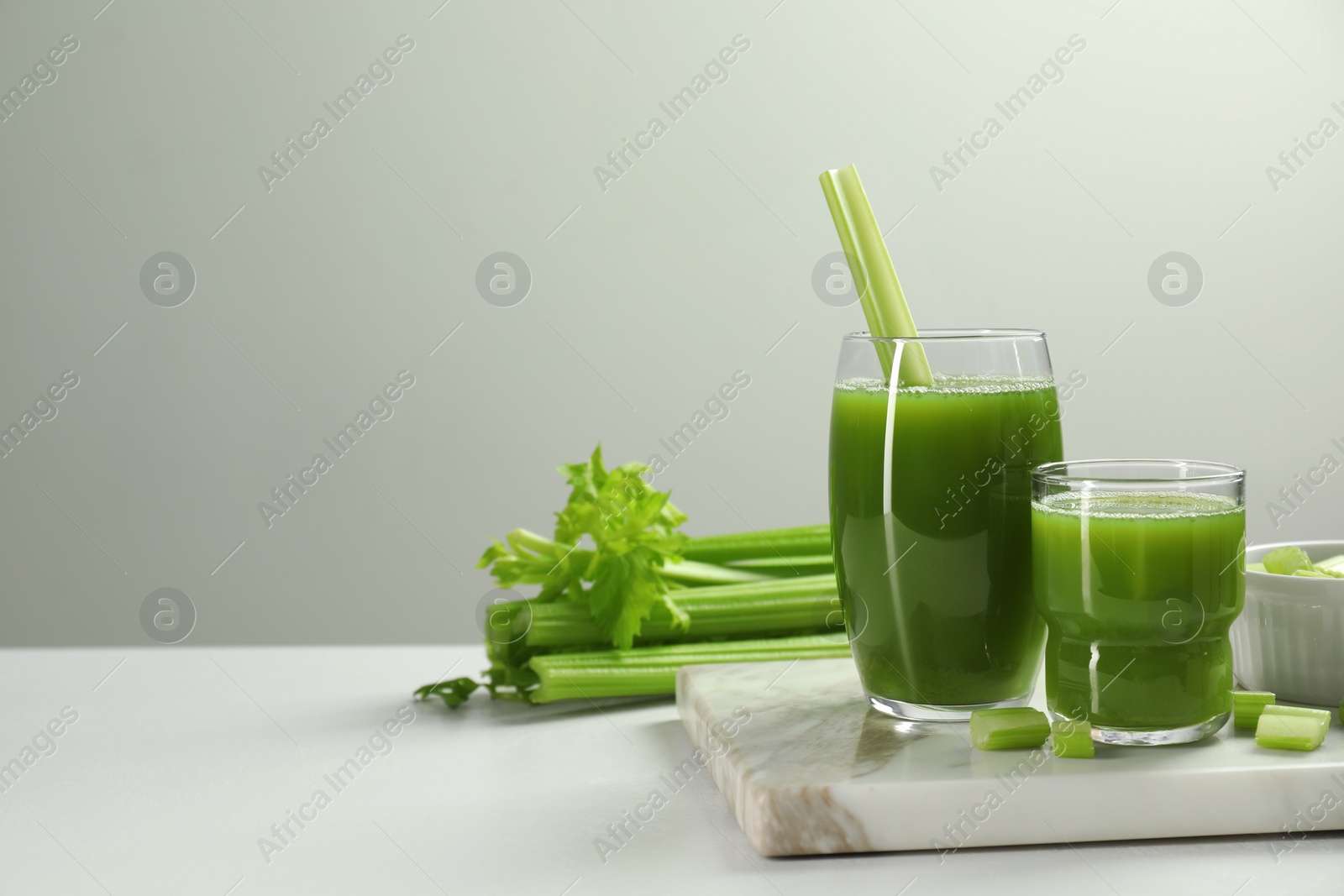 Photo of Glasses of delicious celery juice and vegetables on white table. Space for text