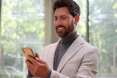 Photo of Positive handsome man using his smartphone indoors