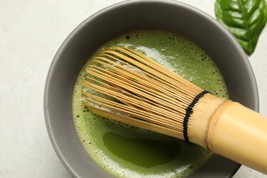 Photo of Cup of fresh green matcha tea with bamboo whisk on light grey table, top view