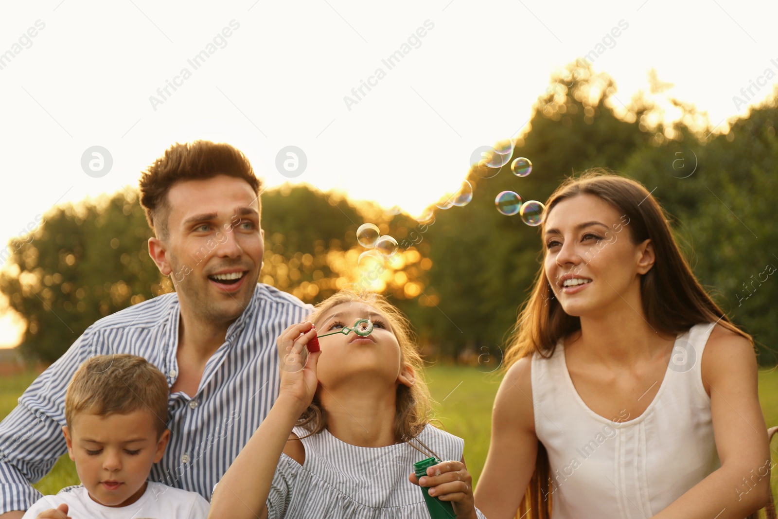 Photo of Happy family blowing soap bubbles in park at sunset. Summer picnic