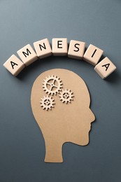 Photo of Wooden cubes with word Amnesia, human head cutout and cogwheels on grey background, top view