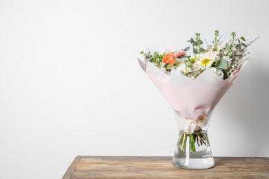 Bouquet of beautiful flowers in vase on wooden table against white wall. Space for text