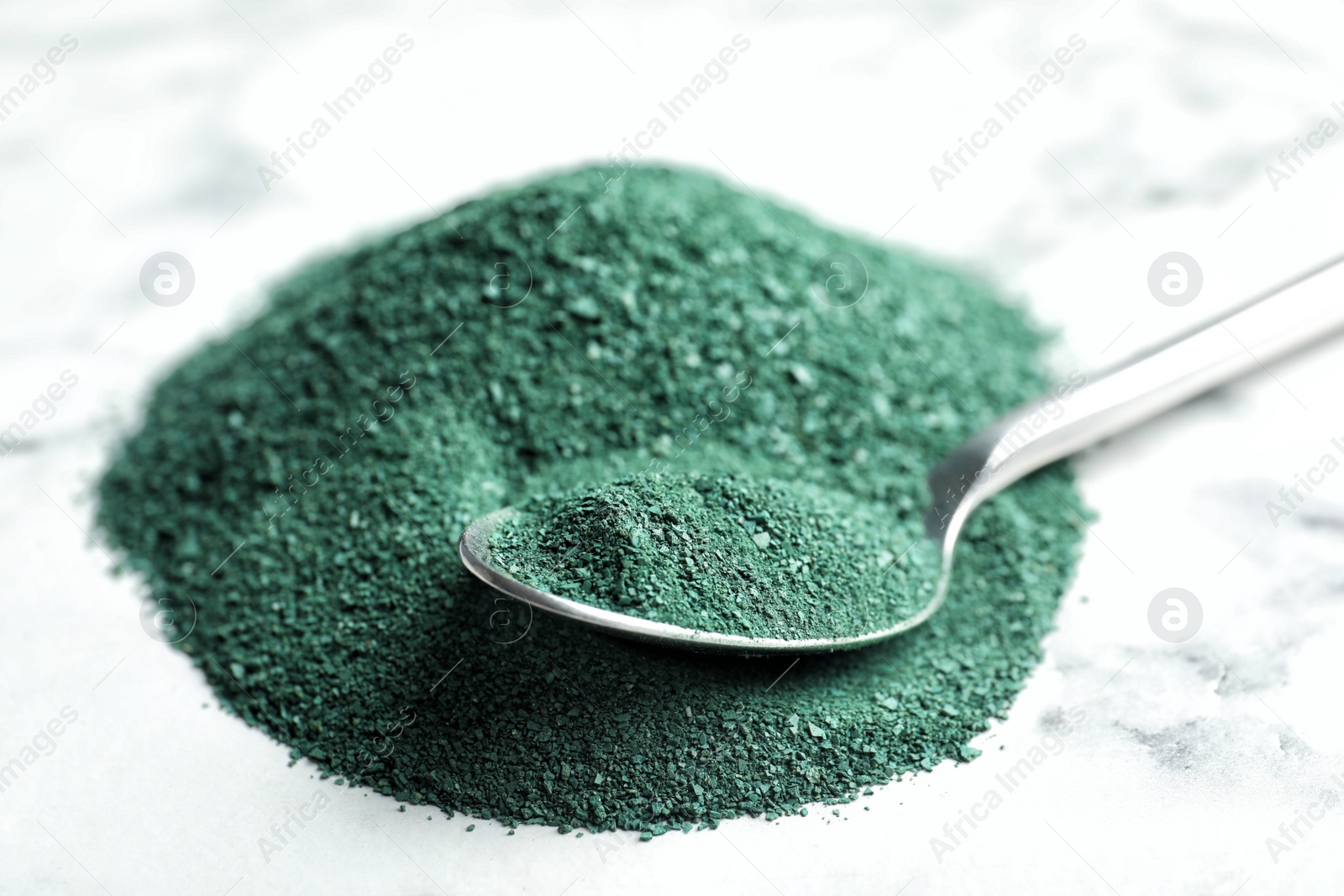 Photo of Spoon and spirulina powder on marble background, closeup