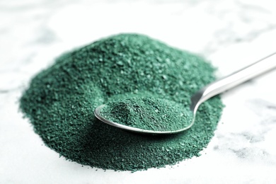 Photo of Spoon and spirulina powder on marble background, closeup
