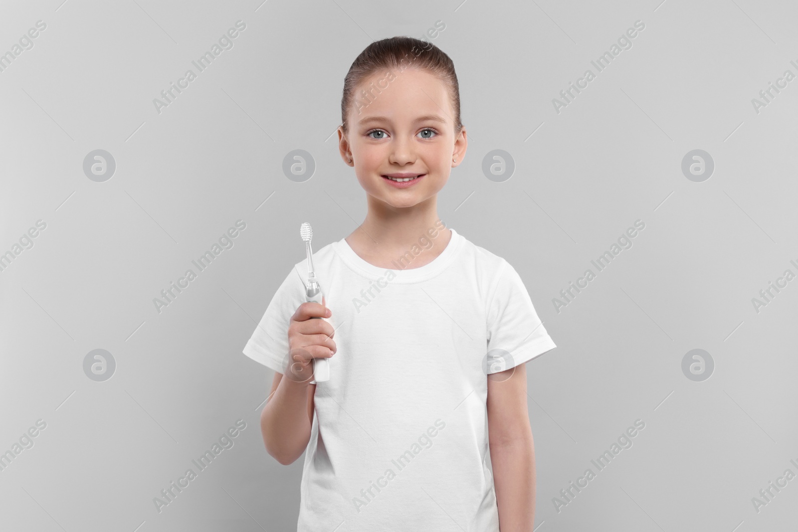 Photo of Happy girl holding electric toothbrush on light grey background