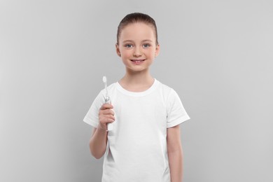 Happy girl holding electric toothbrush on light grey background