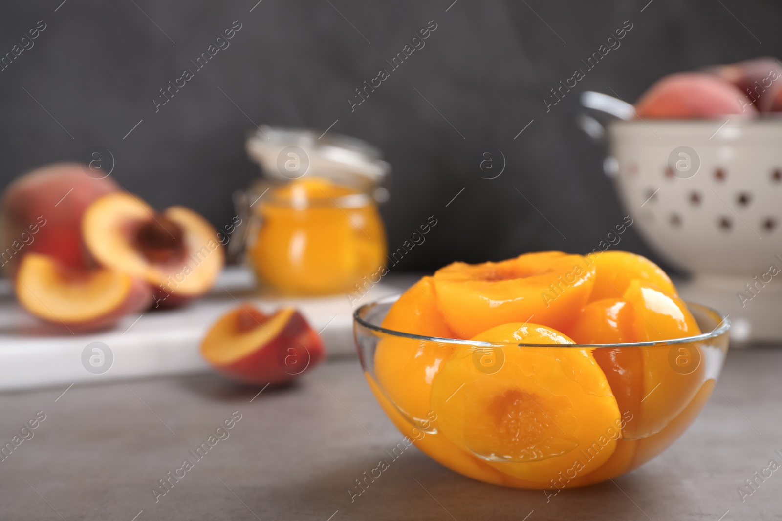 Photo of Glass bowl with conserved peach halves on grey table. Space for text