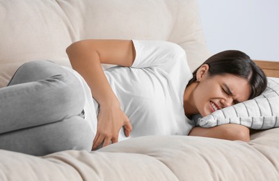 Photo of Young woman suffering from menstrual pain on sofa indoors