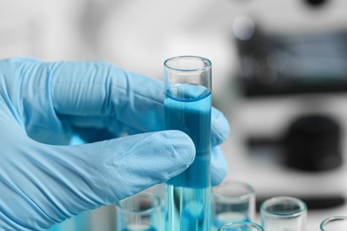 Scientist taking test tube with light blue liquid in laboratory, closeup