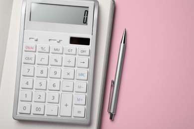 Calculator, notebook and pen on pink background, flat lay with space for text