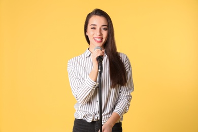 Young woman in casual clothes posing with microphone on color background