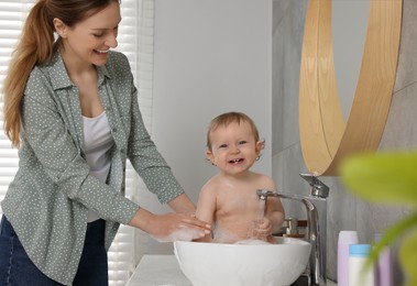 Mother washing her little baby in sink at home