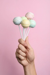 Woman holding sweet cake pops on pink background, closeup