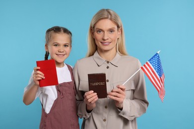Photo of Immigration. Happy woman with her daughter holding passports and American flag on light blue background