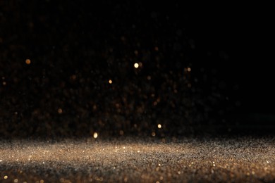 Photo of Shiny golden glitter falling down on black background. Bokeh effect