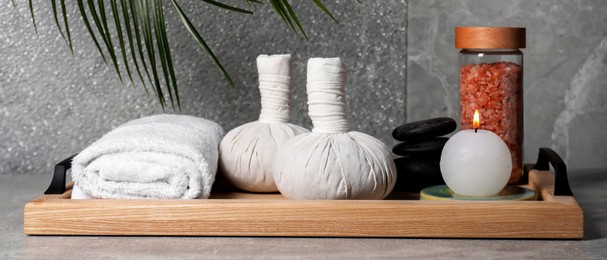 Herbal massage bags, spa stones, sea salt, rolled towel and candle on grey table. Banner design