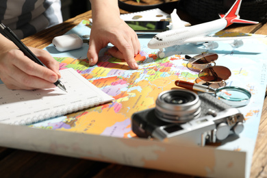 Woman marking calendar at table with world map, closeup. Travel during summer vacation