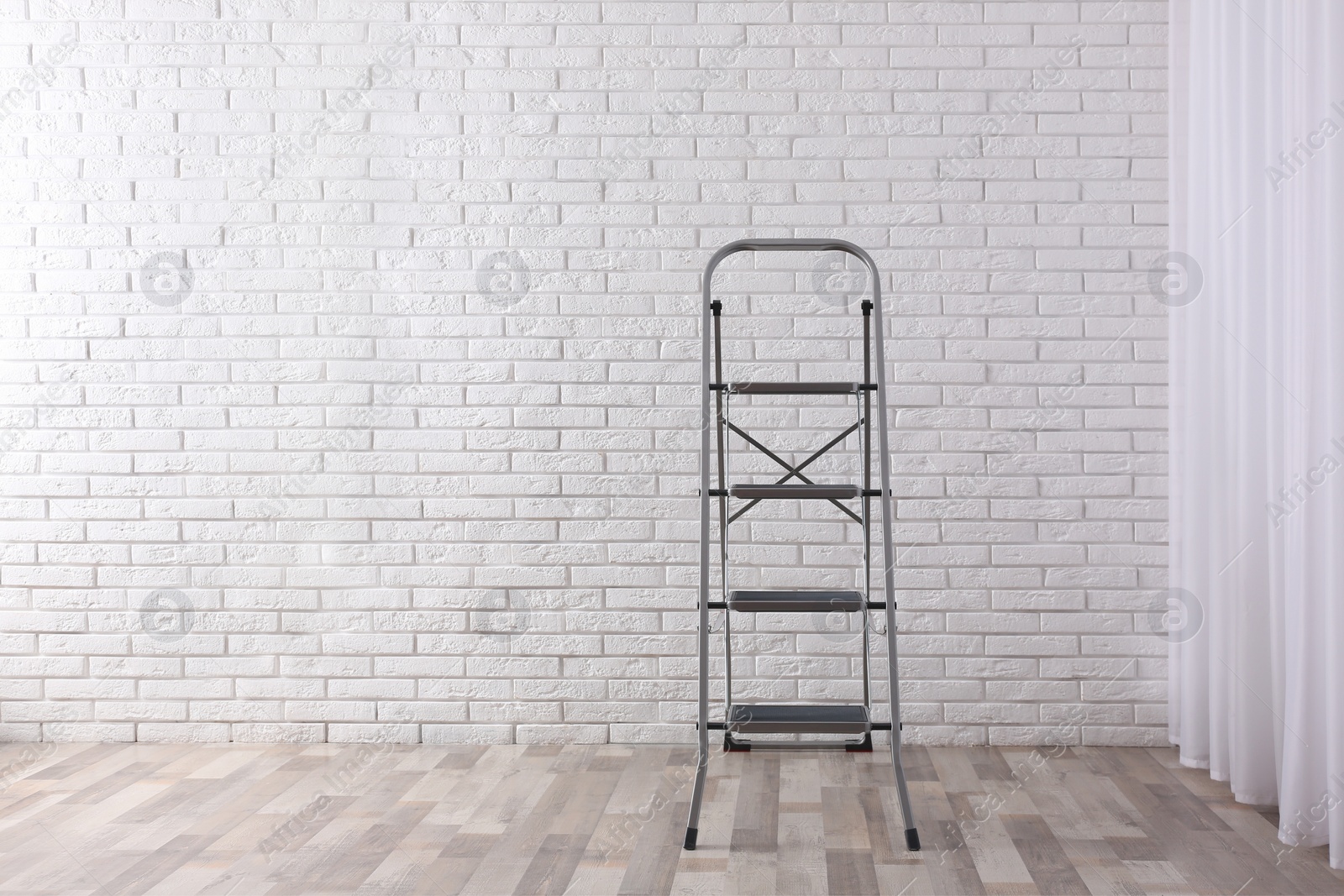 Photo of Modern metal stepladder near white brick wall indoors. Space for text