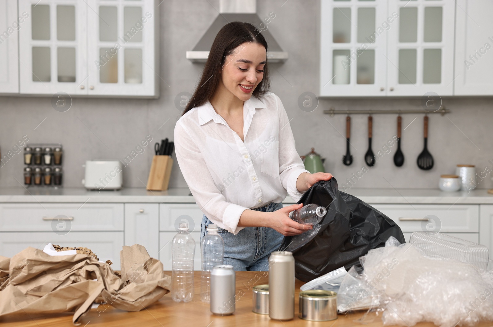 Photo of Smiling woman separating garbage at table in kitchen