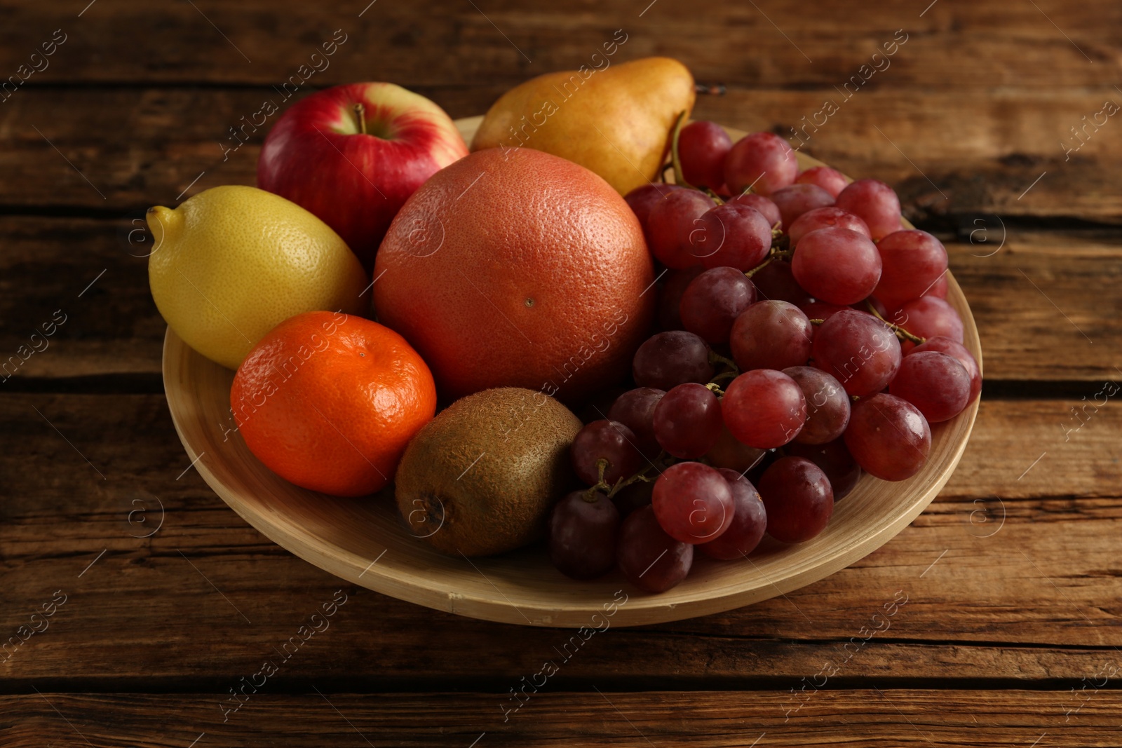 Photo of Fresh ripe fruits in bowl on wooden table, closeup