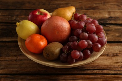 Photo of Fresh ripe fruits in bowl on wooden table, closeup