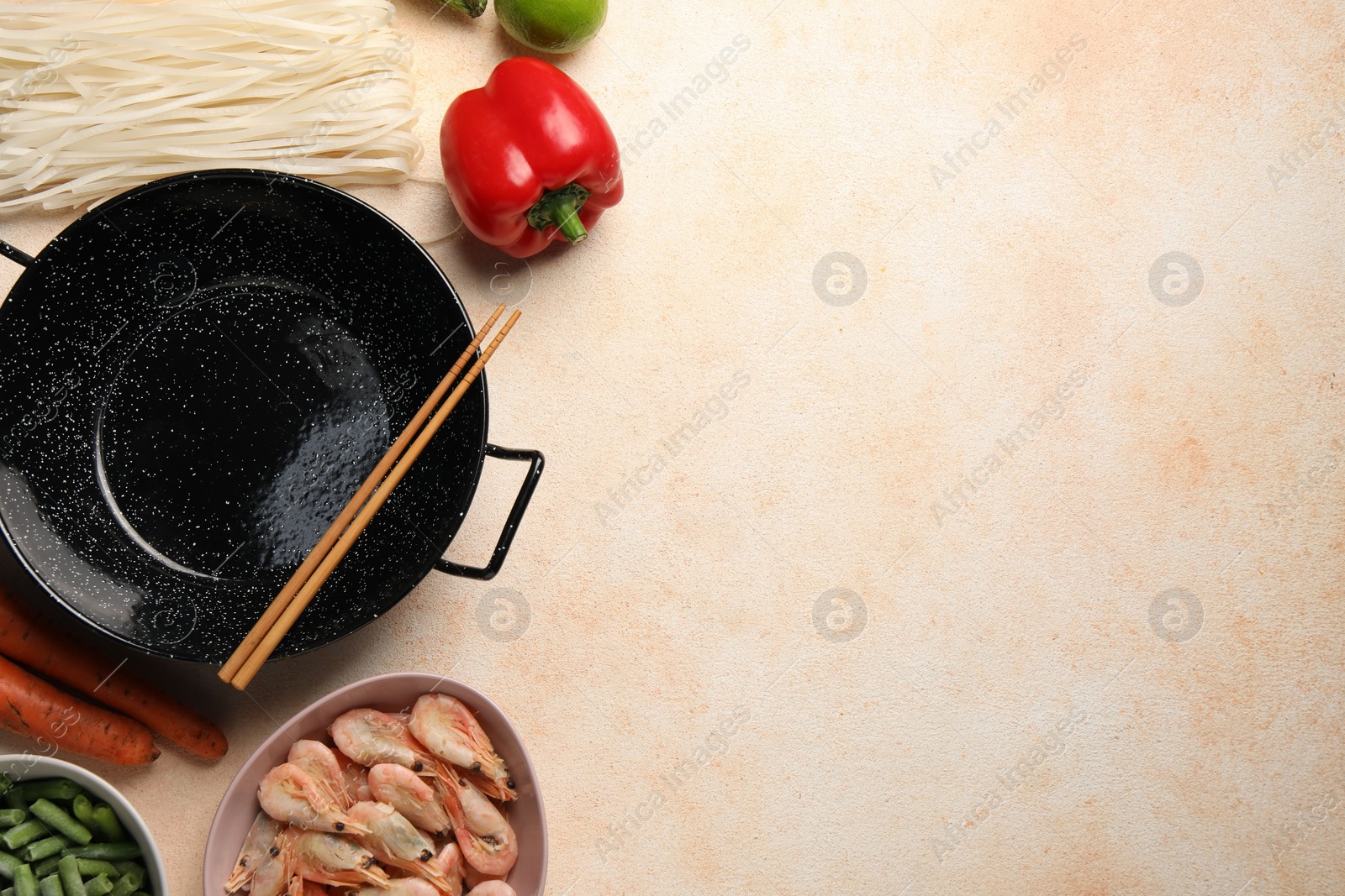 Photo of Black wok, chopsticks and products on color textured table, flat lay. Space for text