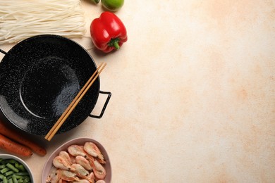 Black wok, chopsticks and products on color textured table, flat lay. Space for text