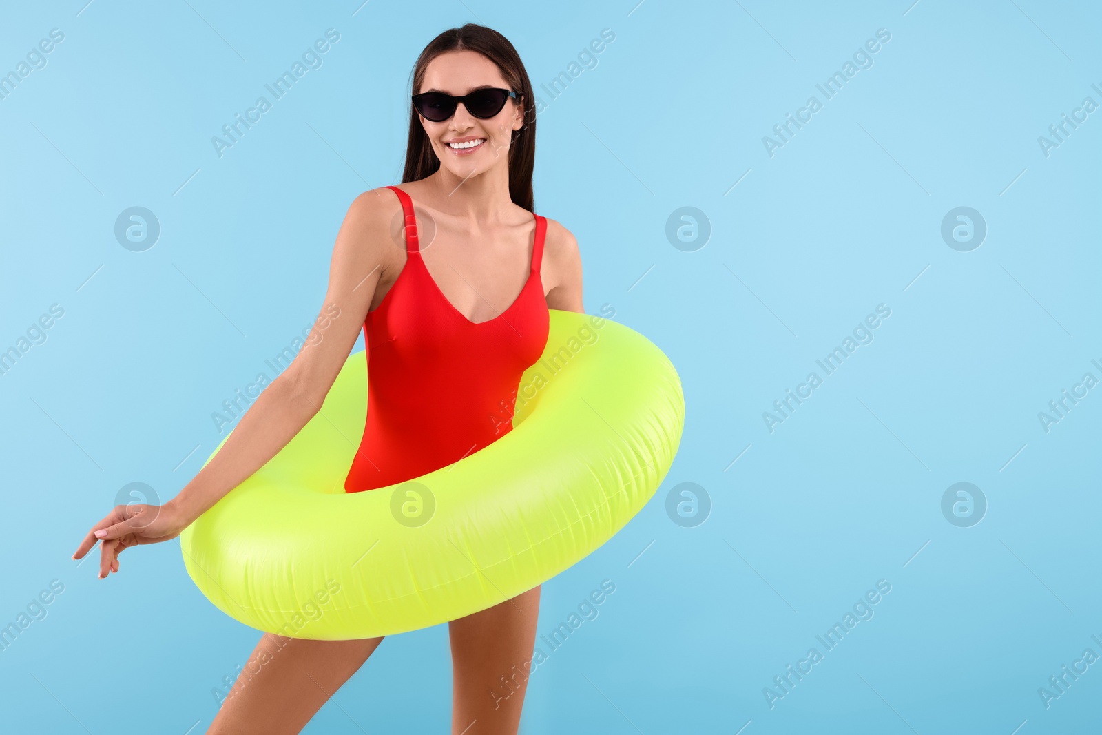 Photo of Young woman in stylish swimsuit with inflatable ring on light blue background, space for text