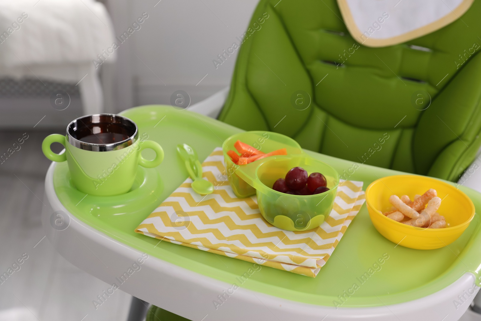 Photo of High chair with food in baby tableware on tray indoors