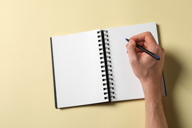 Man with pen and empty notepad on yellow background, top view