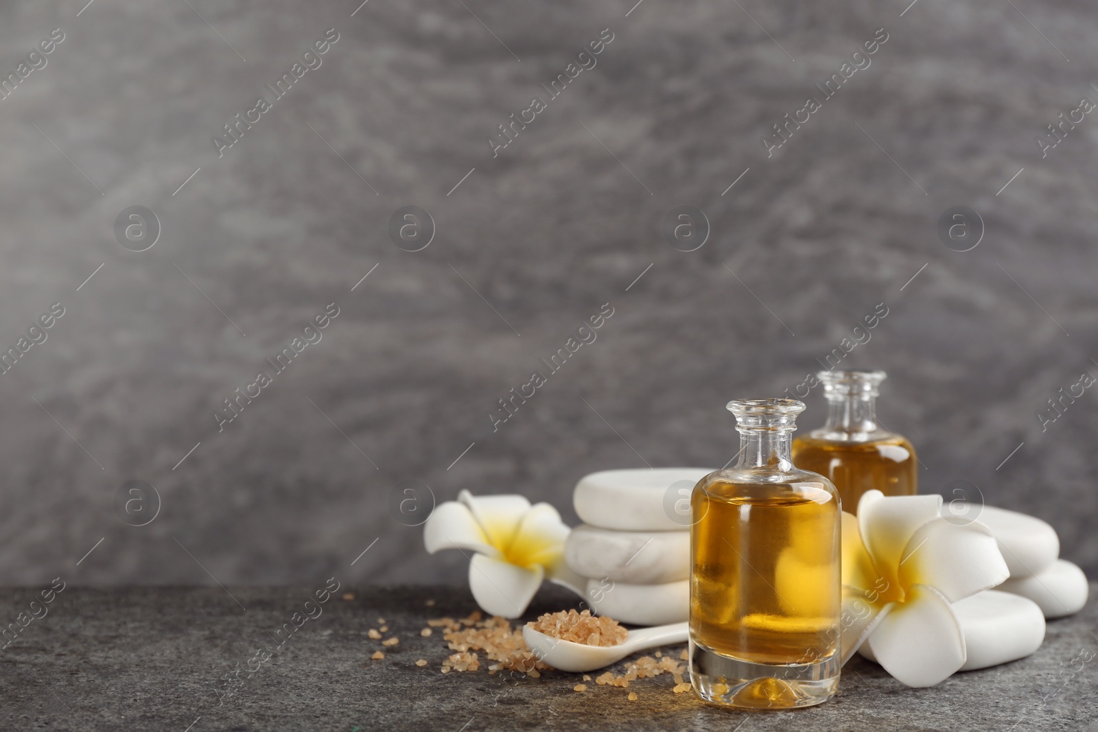 Photo of Beautiful spa composition with essential oil, stones and flowers on grey table. Space for text