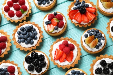 Photo of Many different berry tarts on blue wooden table, flat lay. Delicious pastries