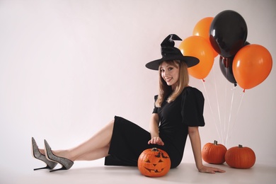 Beautiful woman in witch costume with balloons and pumpkins on white background, space for text. Halloween party