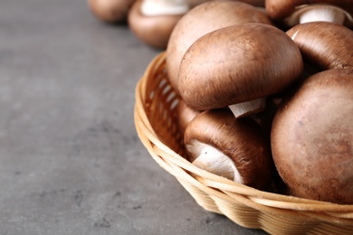 Photo of Wicker bowl of fresh champignon mushrooms on table, closeup. Space for text