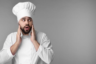 Surprised young chef in uniform on grey background. Space for text